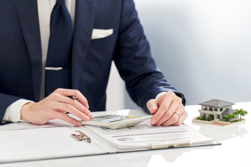 Close-up view of a businessman using a calculator beside a model house on a desk